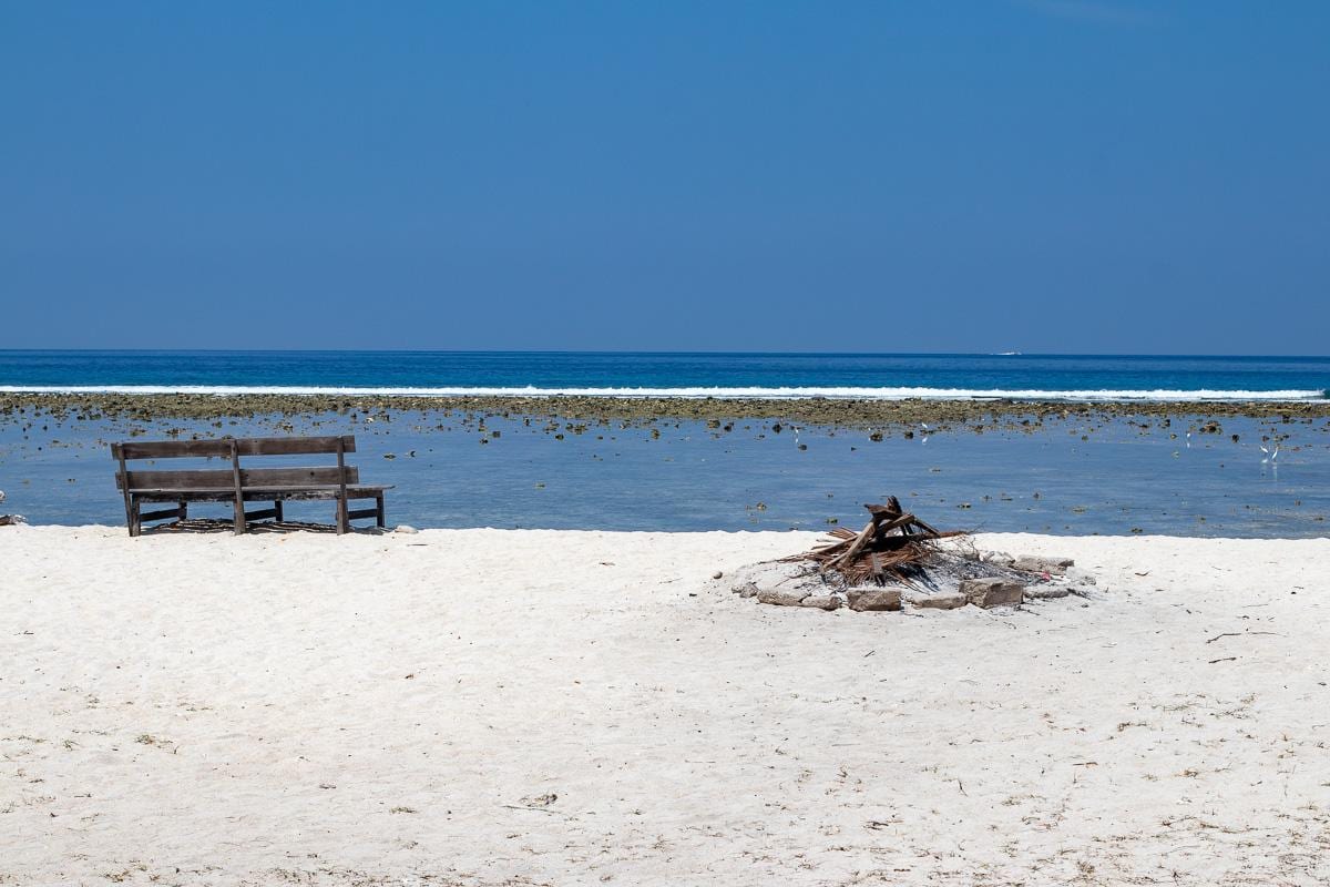 Playa de arena blanca vacía en Gili Trawangan, con un banco de madera frente al arrecife
