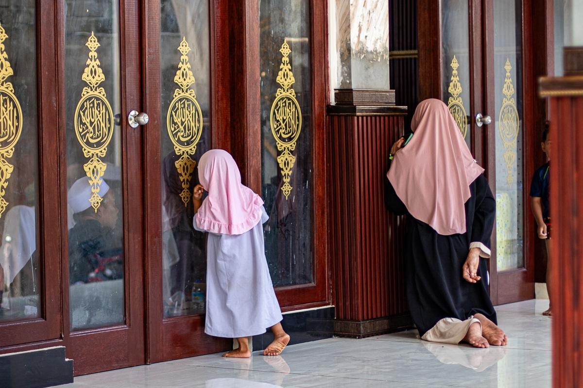 Una niña con hiyab rosa y una mujer junto a las puertas doradas de la mezquita
