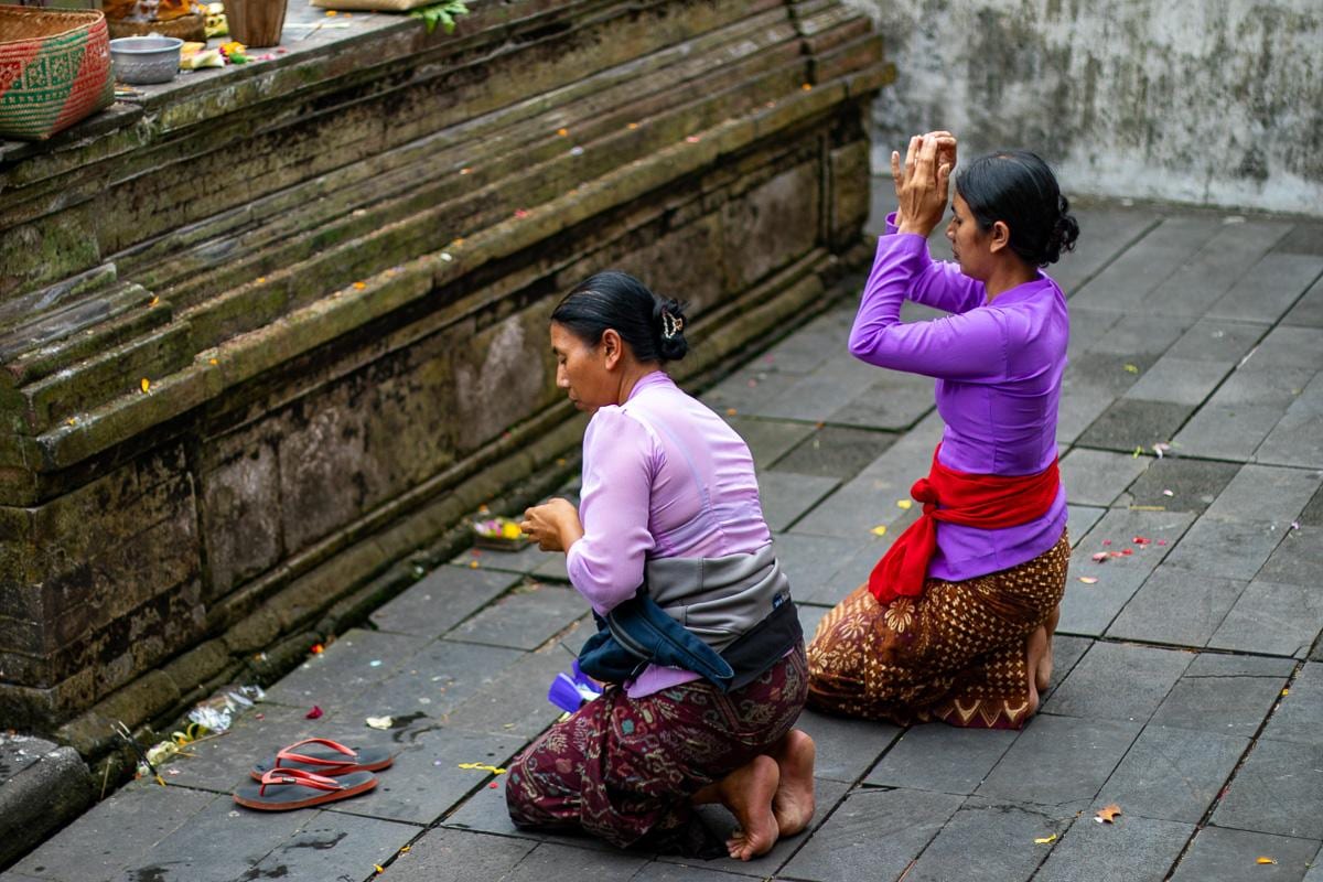 Dos mujeres balinesas rezando de rodillas en el suelo del templo de Tirta Empul